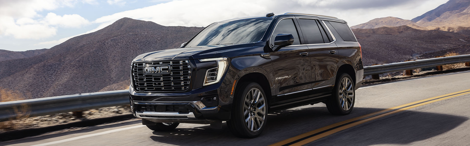 Dark blue GMC Yukon Denali Ultimate SUV driving on a winding mountain road.