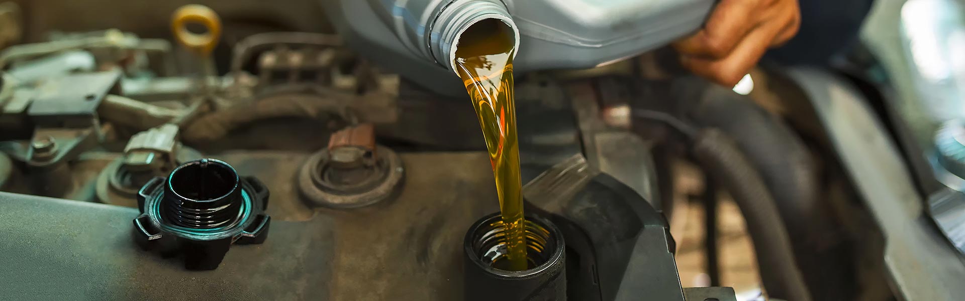Fresh engine oil being poured directly into a car engine bay during maintenance.